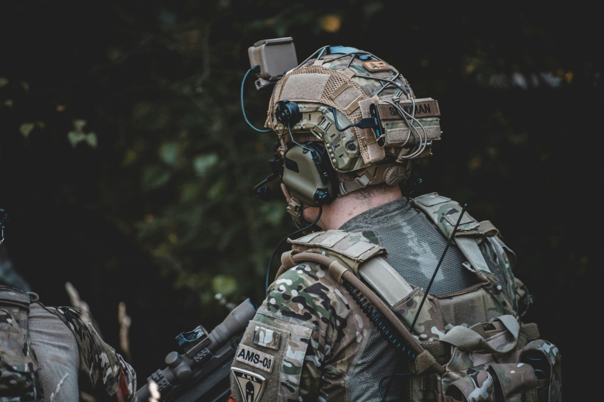 Modern Tactical Gear A close-up image of an individual wearing camouflage clothing and a tactical vest equipped with multiple pouches and accessories.
