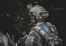 When the Threat Comes from Above: The New Reality of Body Armor A close-up image of an individual wearing camouflage clothing and a tactical vest equipped with multiple pouches and accessories.