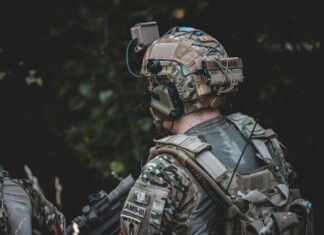 When the Threat Comes from Above: The New Reality of Body Armor A close-up image of an individual wearing camouflage clothing and a tactical vest equipped with multiple pouches and accessories.