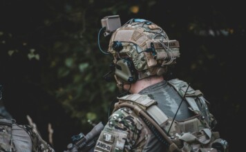 When the Threat Comes from Above: The New Reality of Body Armor A close-up image of an individual wearing camouflage clothing and a tactical vest equipped with multiple pouches and accessories.